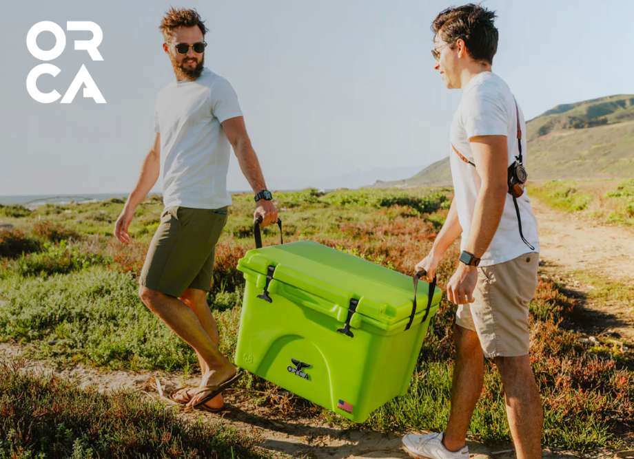 Two men carrying a green cooler to the beach