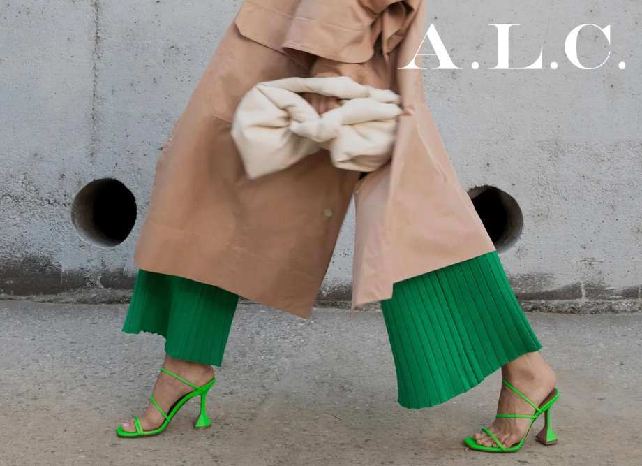 Woman in green heels, green pants, and a tan trench coat walking down the street