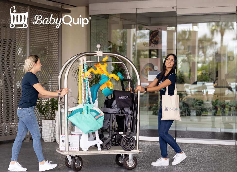 Women pushing a luggage cart that has a stroller, toys and baby essentials on it