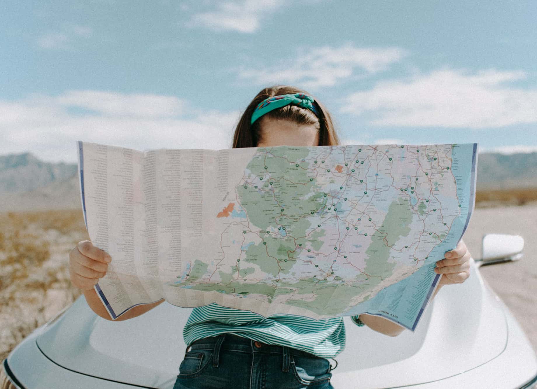 Girl holding map on top of car. 